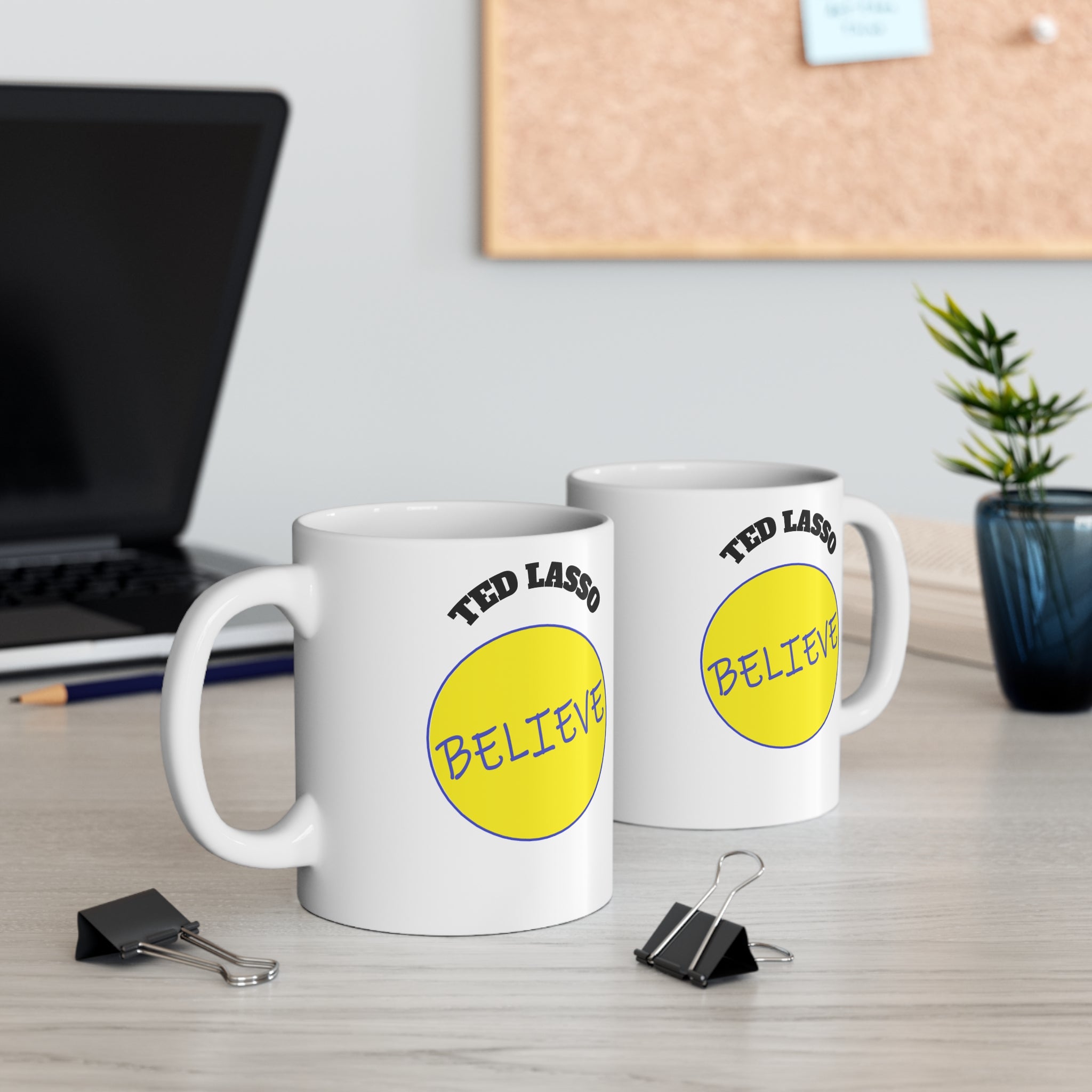 Two white mugs with yellow circular designs and 'Ted Lasso Believe' text on a desk.