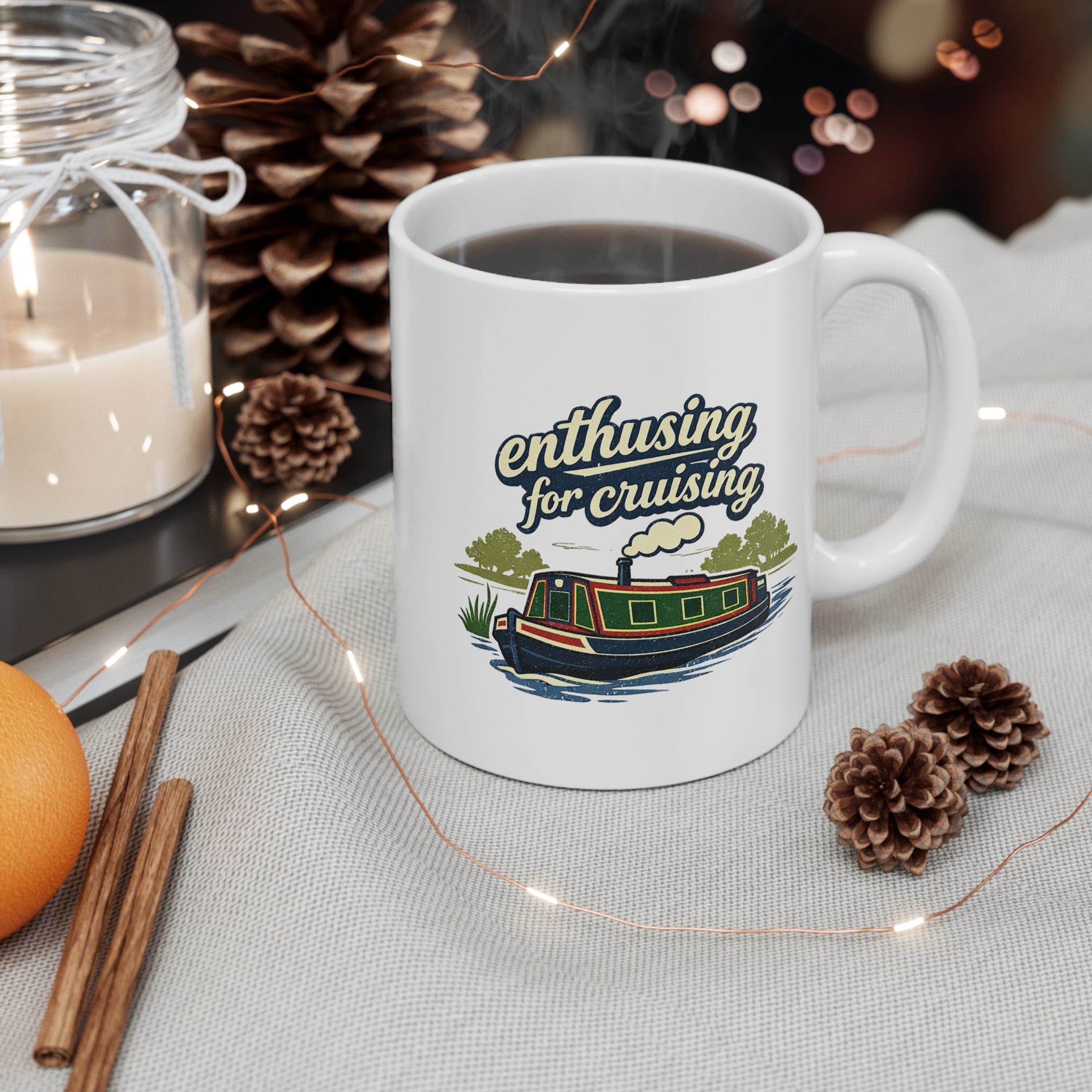 White mug with 'enthusiastic for cruising' design on a table with candles and pinecones.