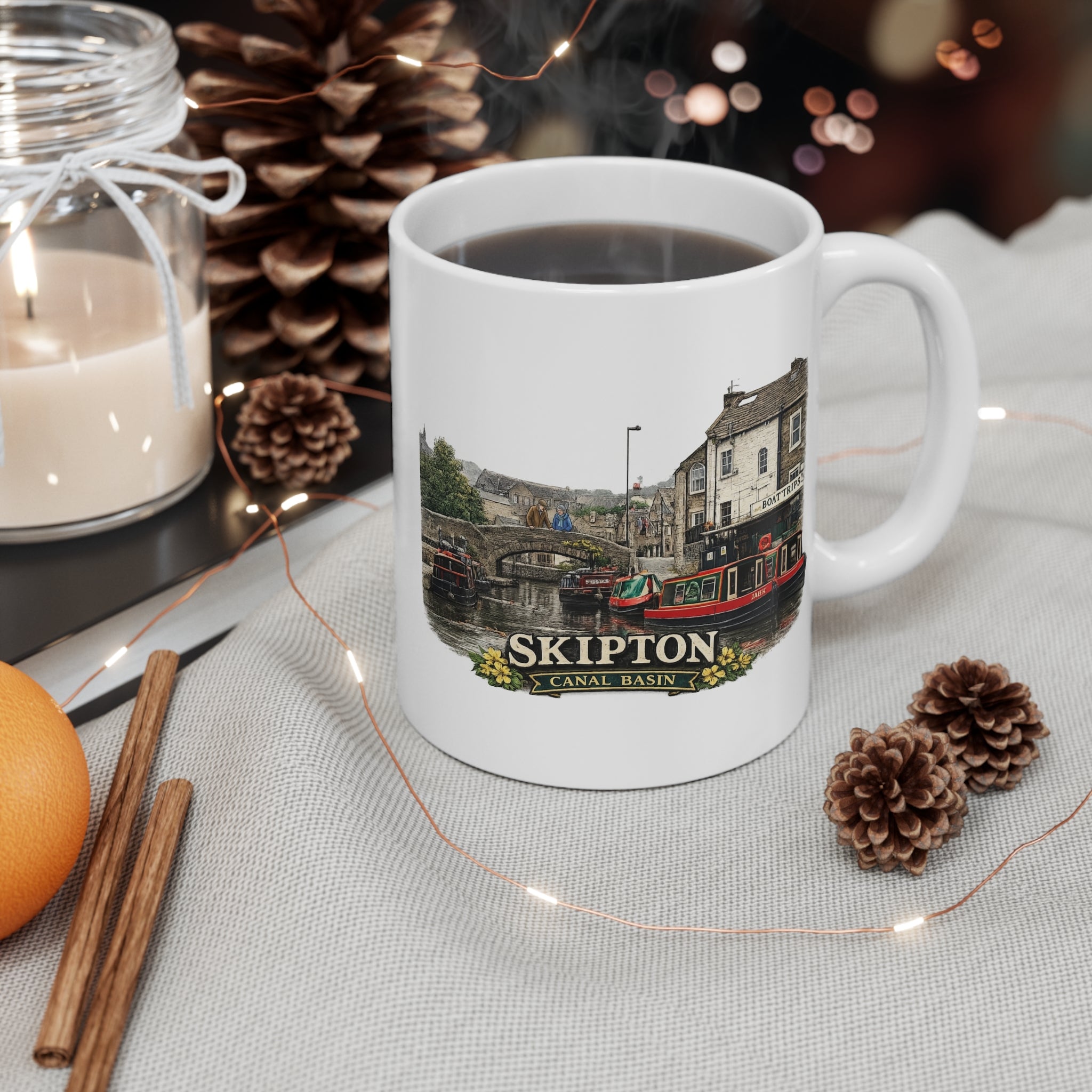 White mug with a Skipton canal basin design on a table with decorative items.