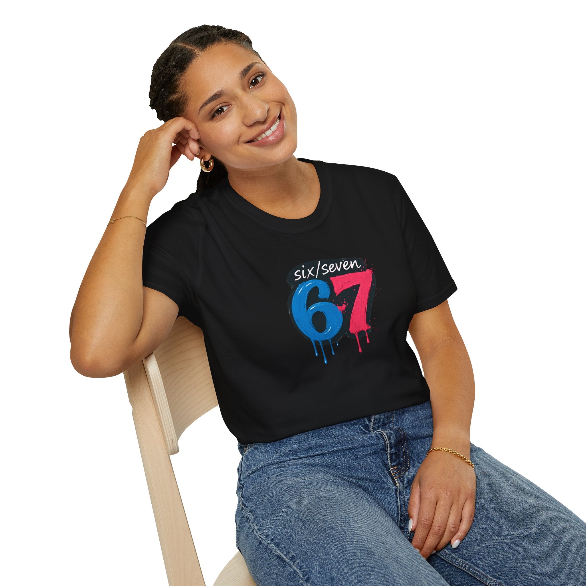 A woman wearing a black t-shirt with colourful six seven oil paint  design sitting on a chair.