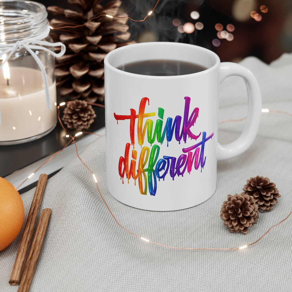 White mug with 'think different' in colorful letters on a table with a candle, cinnamon sticks, and pine cones.
