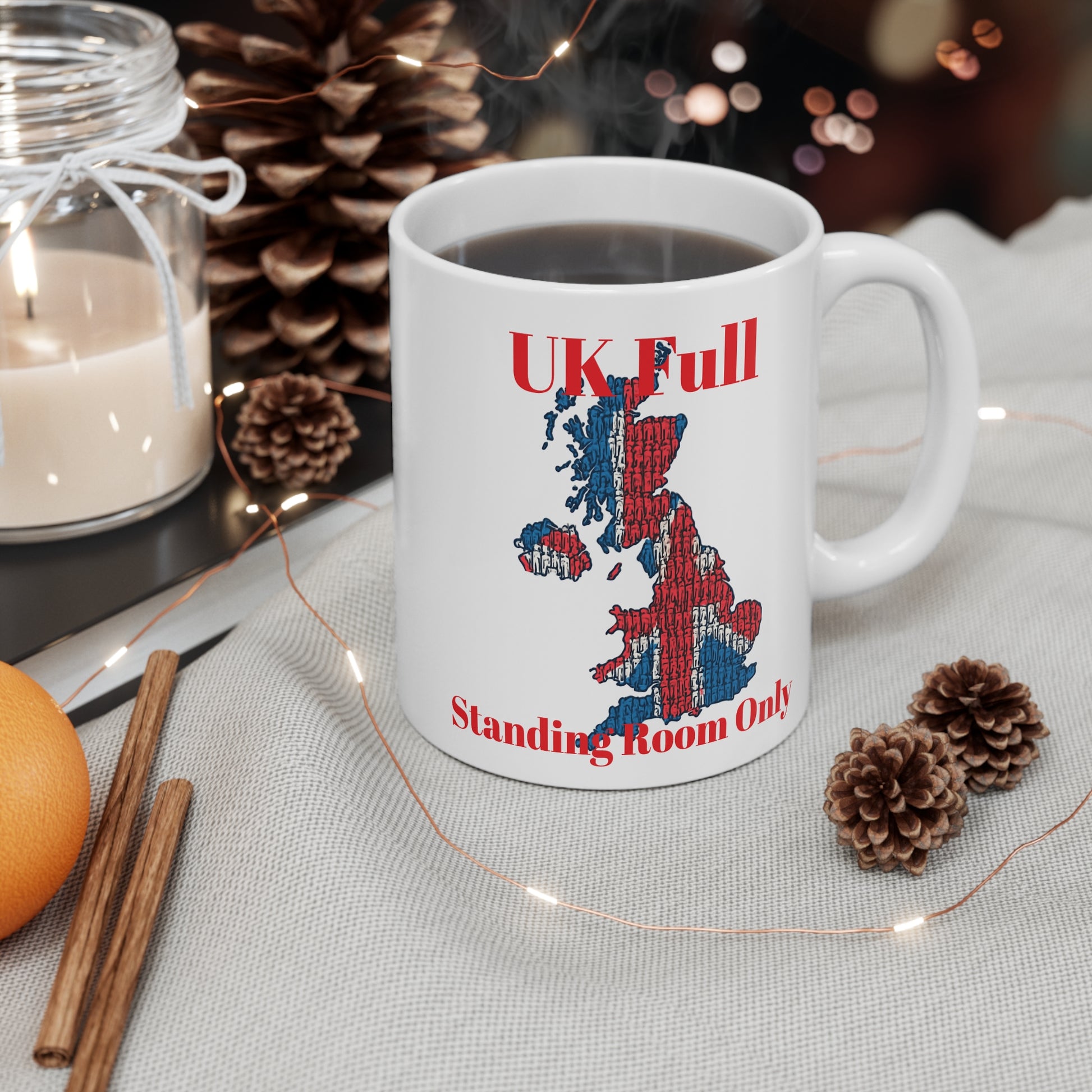 White mug with UK map design  and text, UK full standing room only surrounded by decorative items on a table.