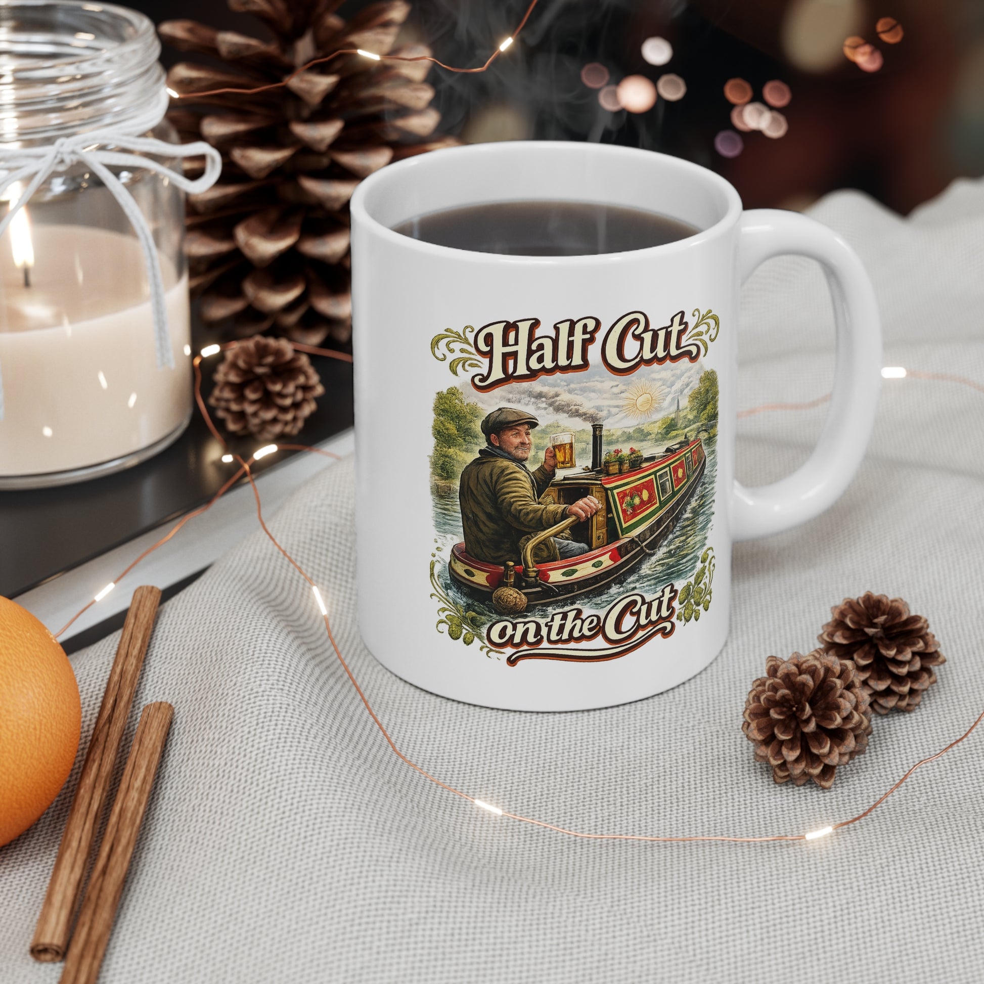 White mug with 'Half Cut on the Cut' design, surrounded by decorative items like a candle, cinnamon sticks, and pine cones.