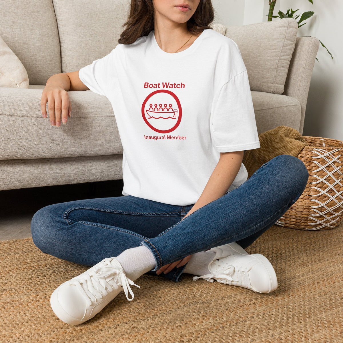 Person wearing a white t-shirt with a red graphic and text, sitting on the floor in a living room.