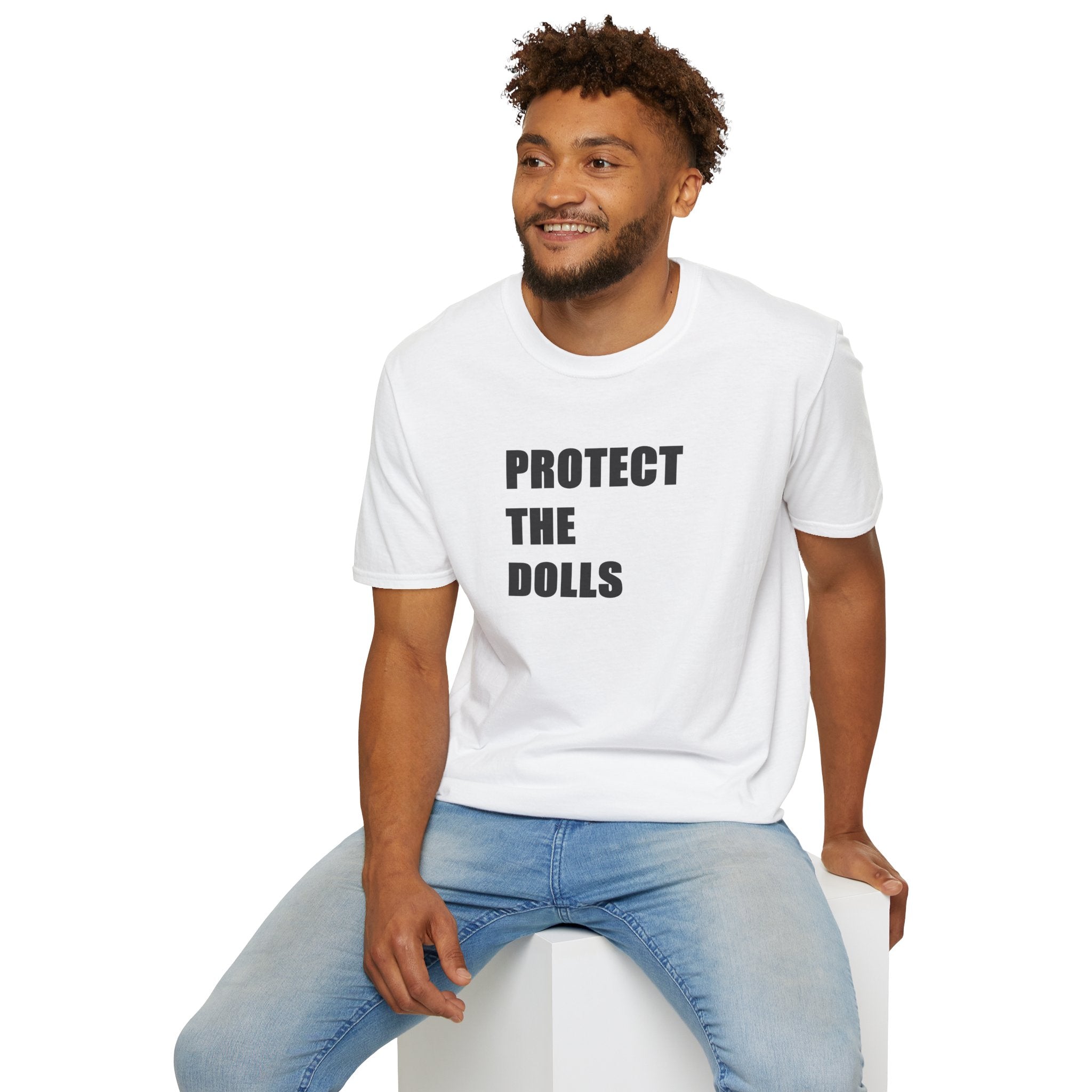 Man wearing a white t-shirt with 'PROTECT THE DOLLS' text, sitting on a white stool against a white background.