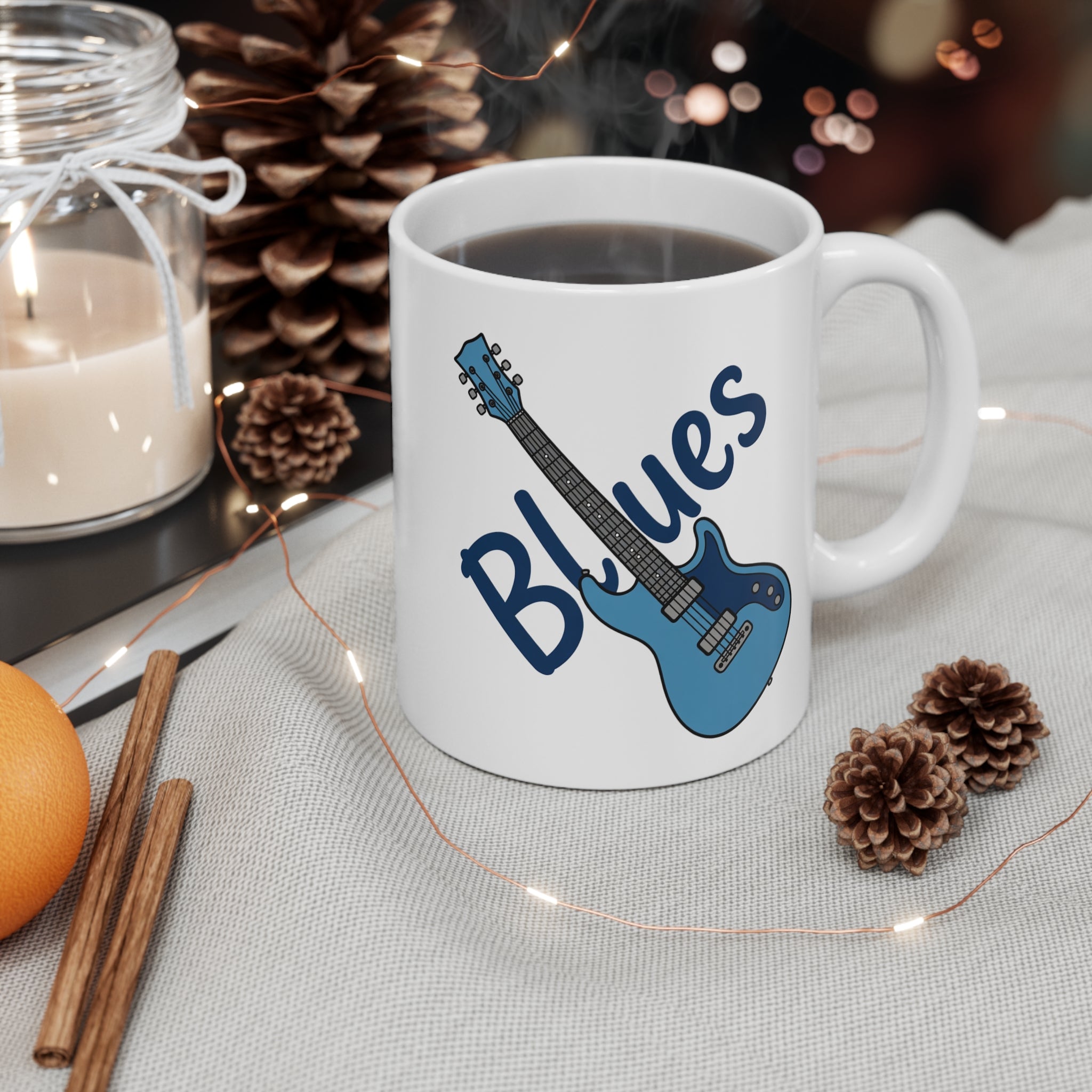 White mug with blue guitar design and 'Blues' text, surrounded by decorative items on a table.