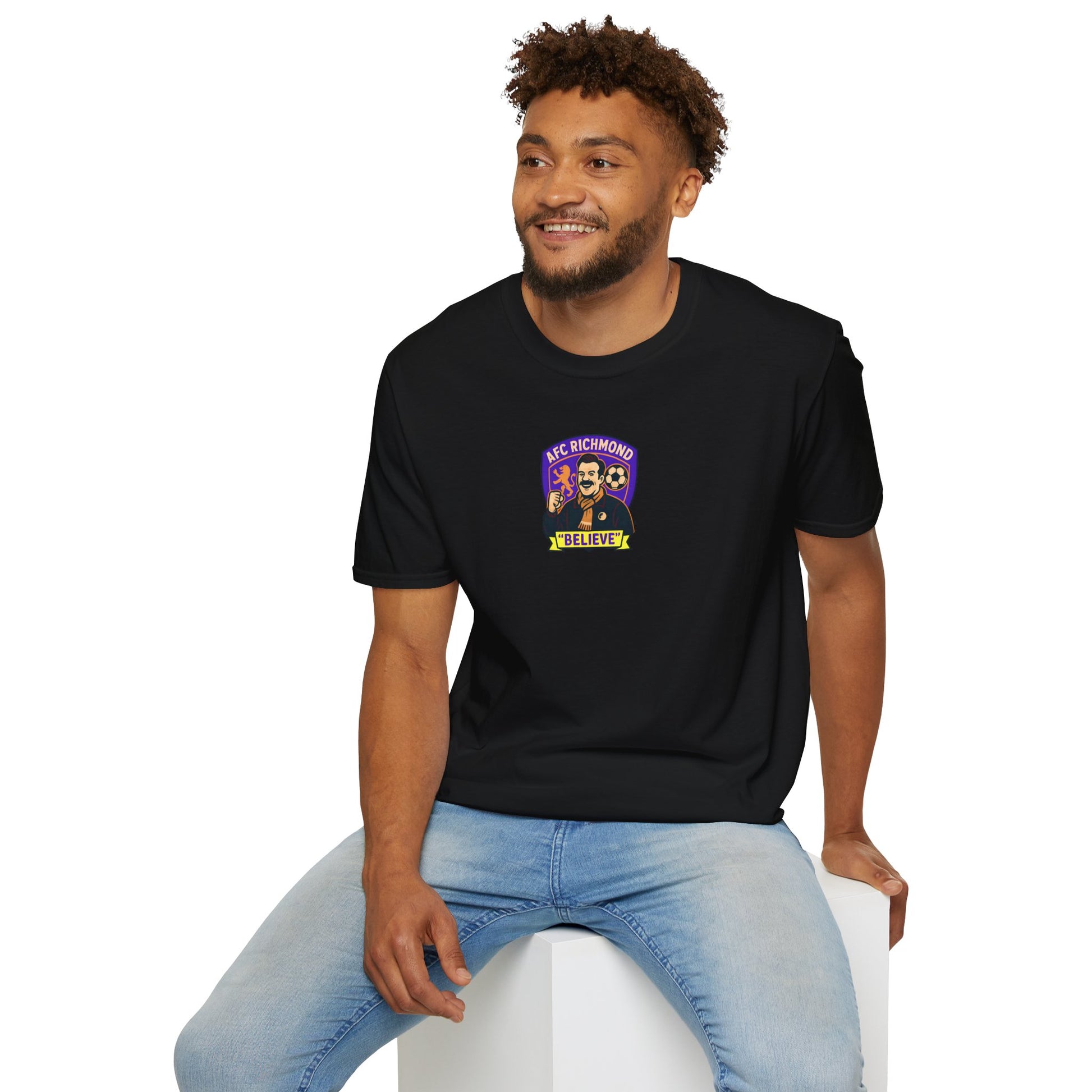 Man wearing a black t-shirt with a AFC Richmond logo sitting on a white stool against a white background