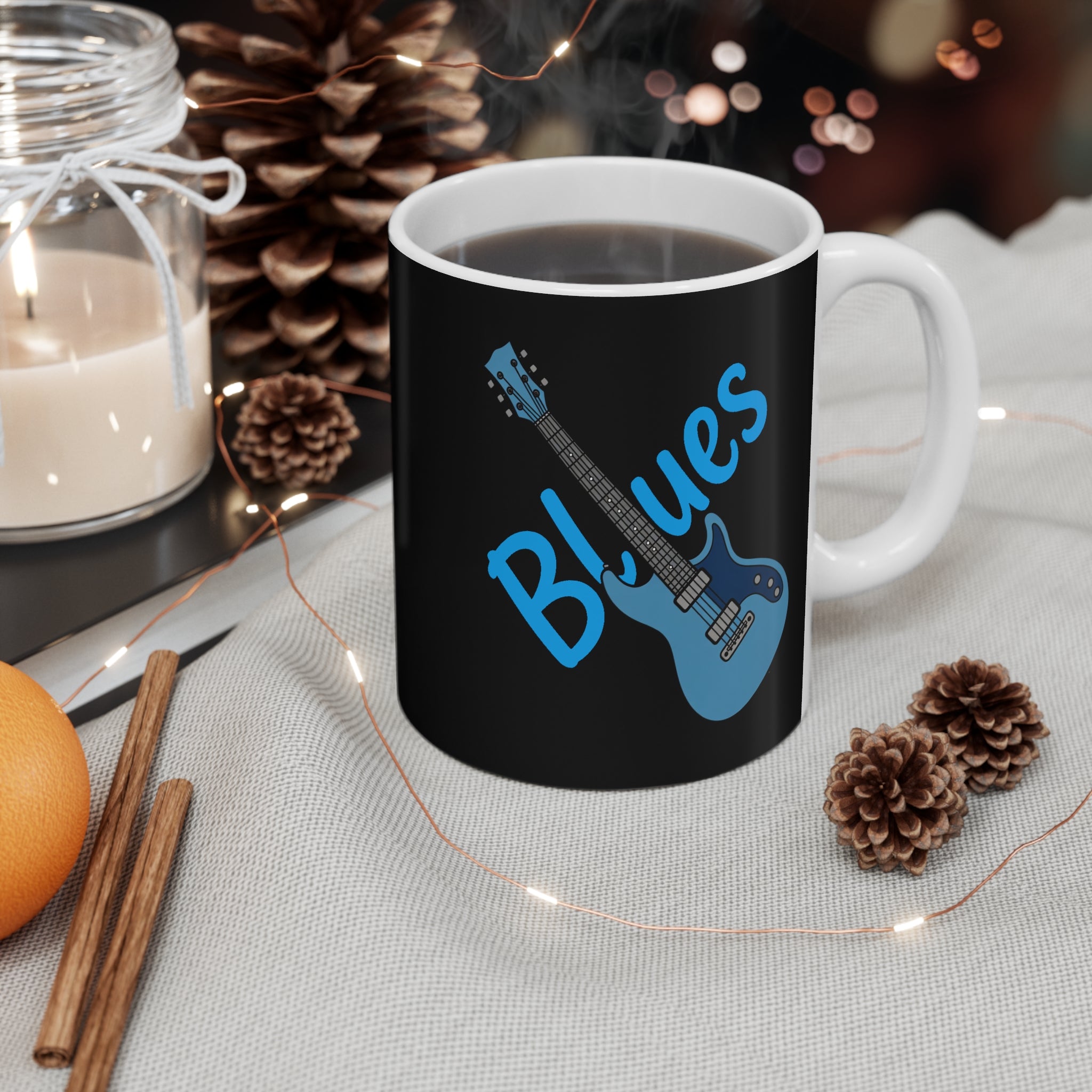 Black mug with blue guitar design and 'Blues' text on a table with decorative items.