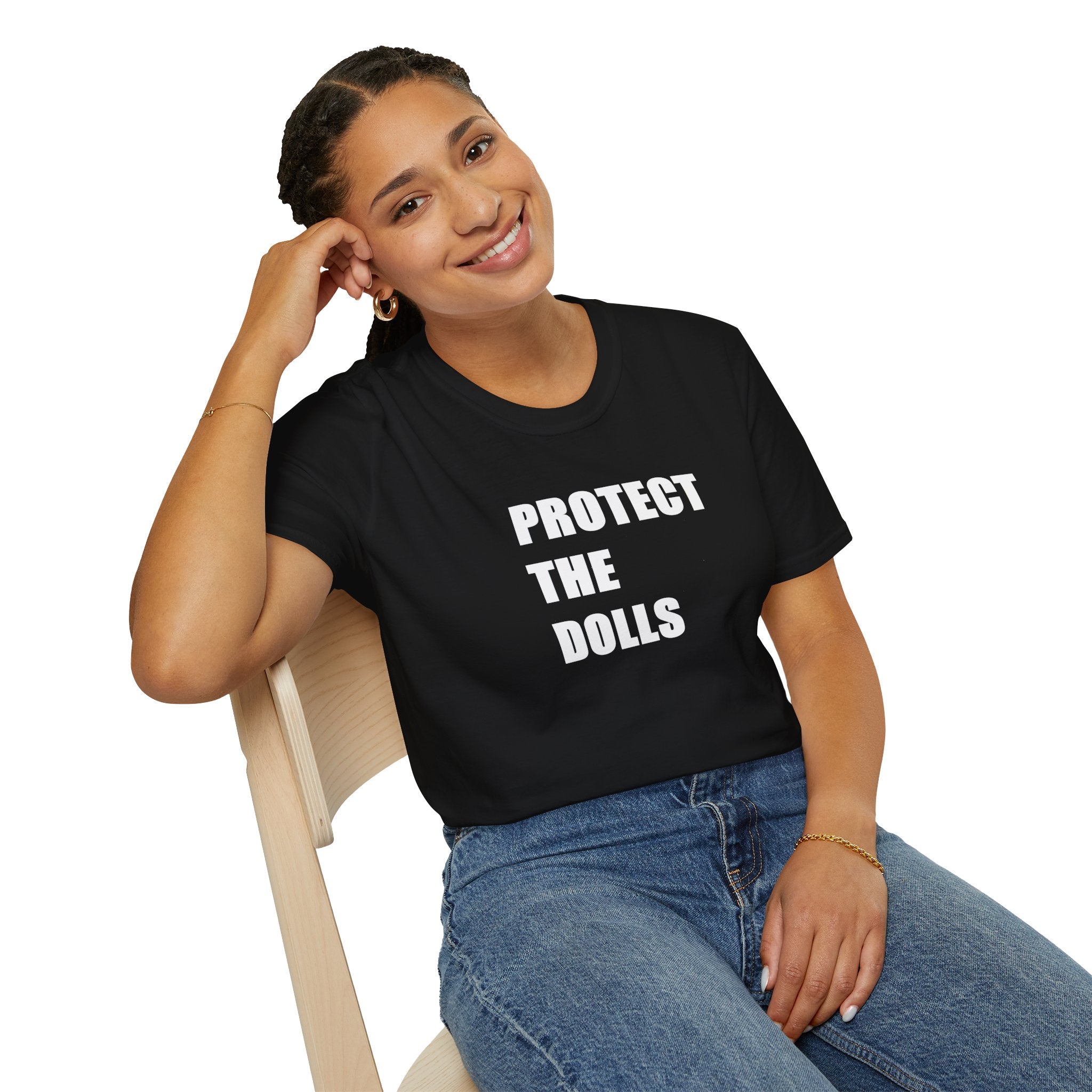Person wearing a black t-shirt with 'PROTECT THE DOLLS' text, sitting on a chair.