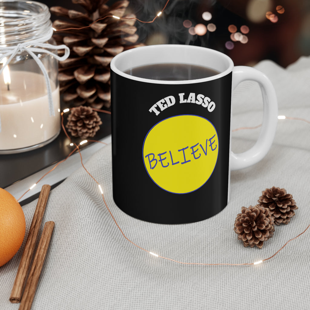 Black mug with 'Ted Lasso Believe' design on a table with decorative items