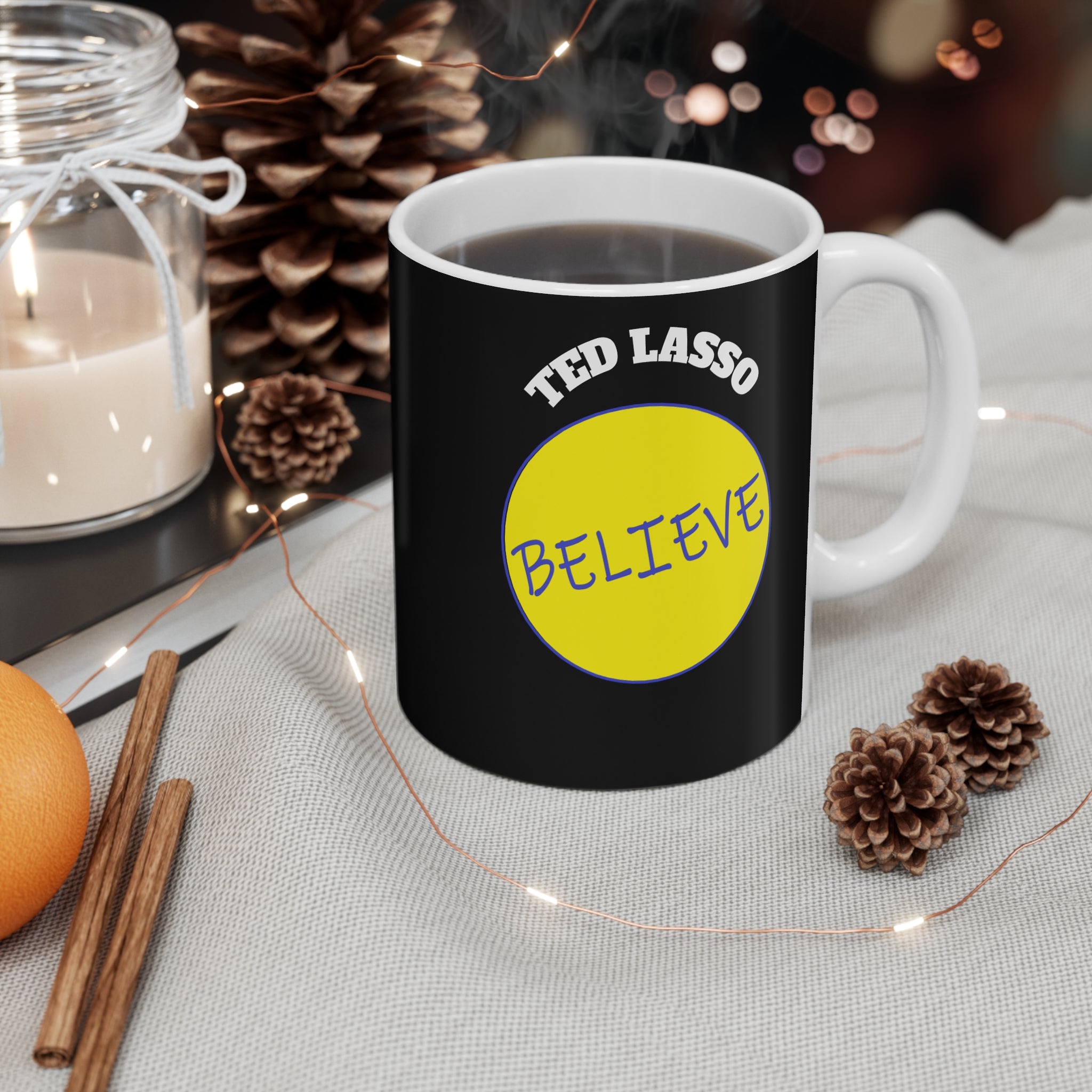 Black mug with 'Ted Lasso Believe' design on a table with decorative items