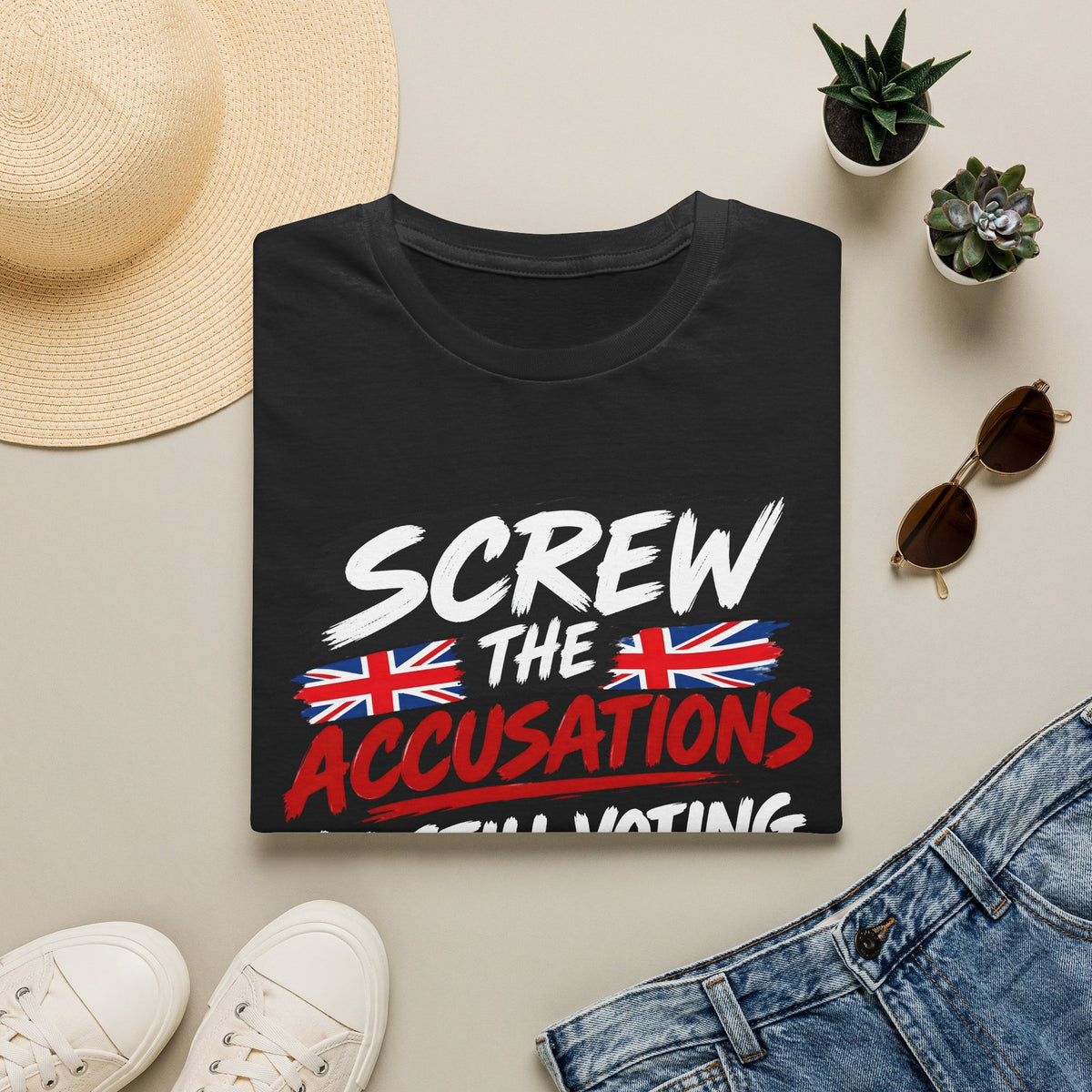 A folded black graphic T-shirt is displayed in a styled flat lay on a light beige surface. The shirt features the text 'SCREW THE ACCUSATIONS I WILL VOTING' in white and red, with two Union Jack flags.