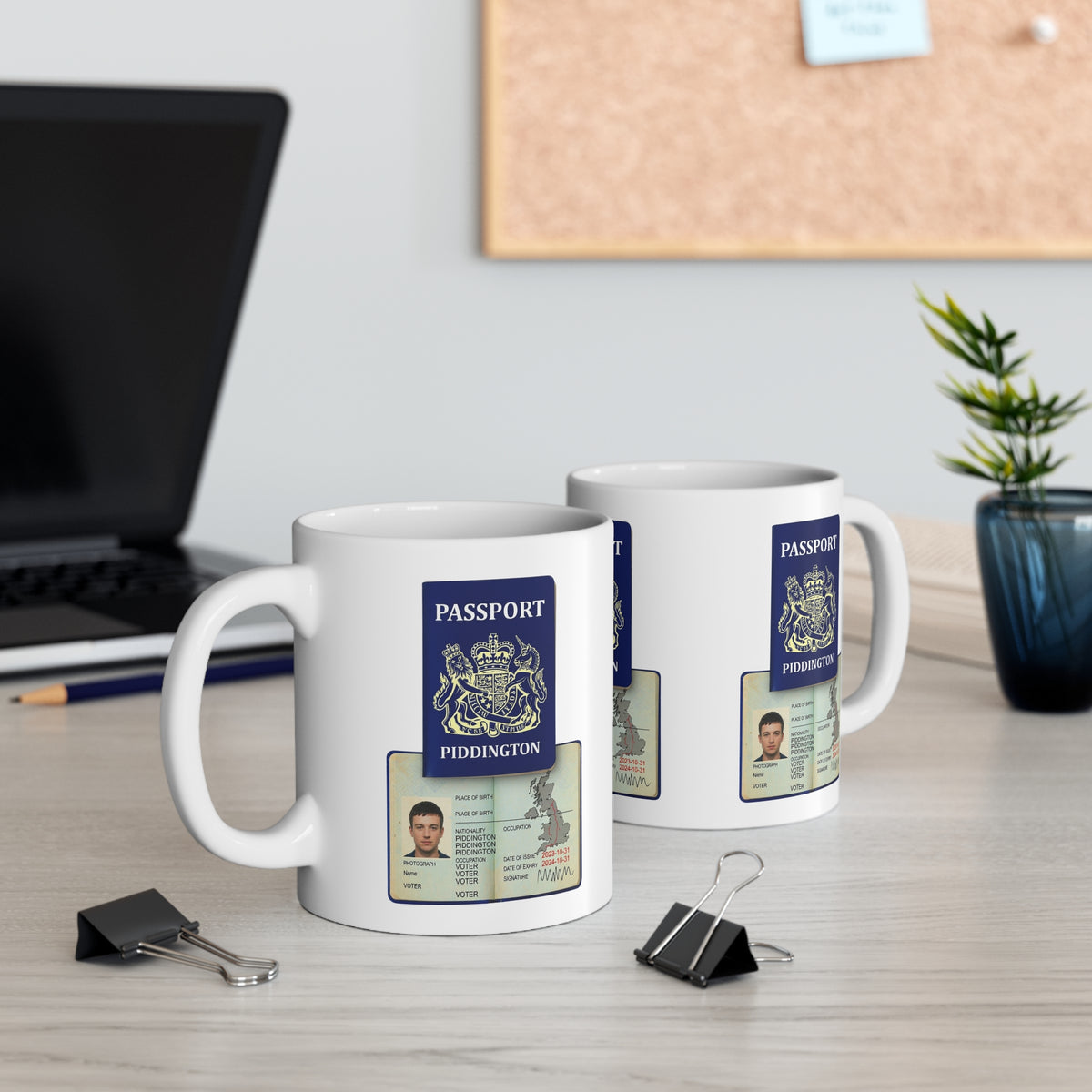 Two white ceramic mugs printed with a fake UK passport design, displayed on a light wood desk in an office setting with a laptop, binder clips, and a plant in the background.