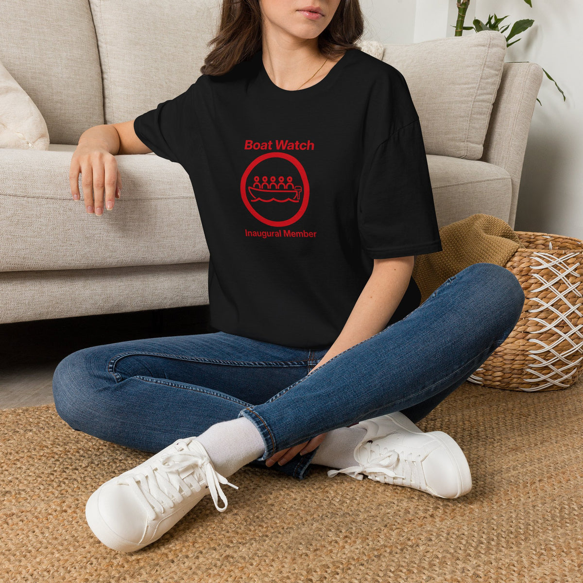 Person wearing a black t-shirt with a colorful graphic design, sitting on the floor in a living room.