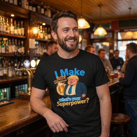 A smiling man standing at a bar wearing a black graphic t-shirt with a cartoon illustration and the text 'I Make Beer Disappear what's your Superpower?'. The background shows a warmly lit, busy pub interior with wooden shelves, bottles, and other patrons.