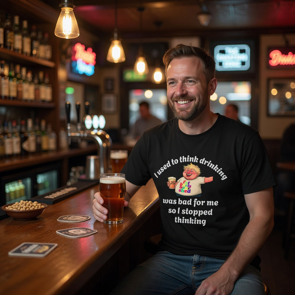 Man sitting at a bar holding a beer, wearing a black t-shirt with humorous text.
