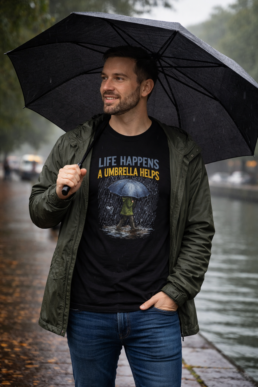 Man holding a black umbrella wearing a t-shirt with a graphic and text. LIFE HAPPENS A UMBRELLA HELPS