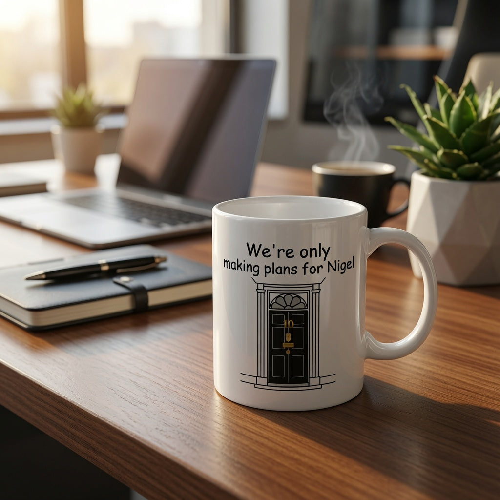 A white ceramic coffee mug with a black graphic of 10 DOWNING STREET door and the text 'We're only making plans for Nigel!' sits on a wooden desk in a blurred office setting with a laptop, notebook, and plants.
