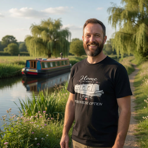 Man wearing a black t-shirt with a boat design and graphic home is where I moor it. Standing by a canal with a boat in the background.