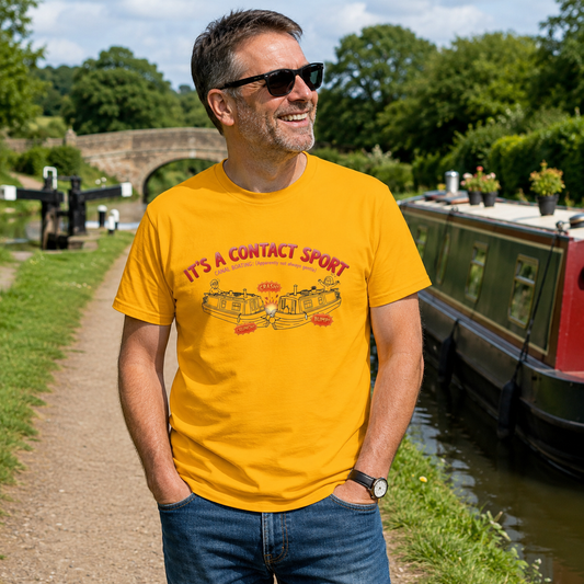 A man wearing a bright yellow graphic canal boat t-shirt with red and black text reading 'IT'S A CONTACT SPORT' and a boat illustration, standing outdoors next to a canal with a narrowboat and green trees in the background.