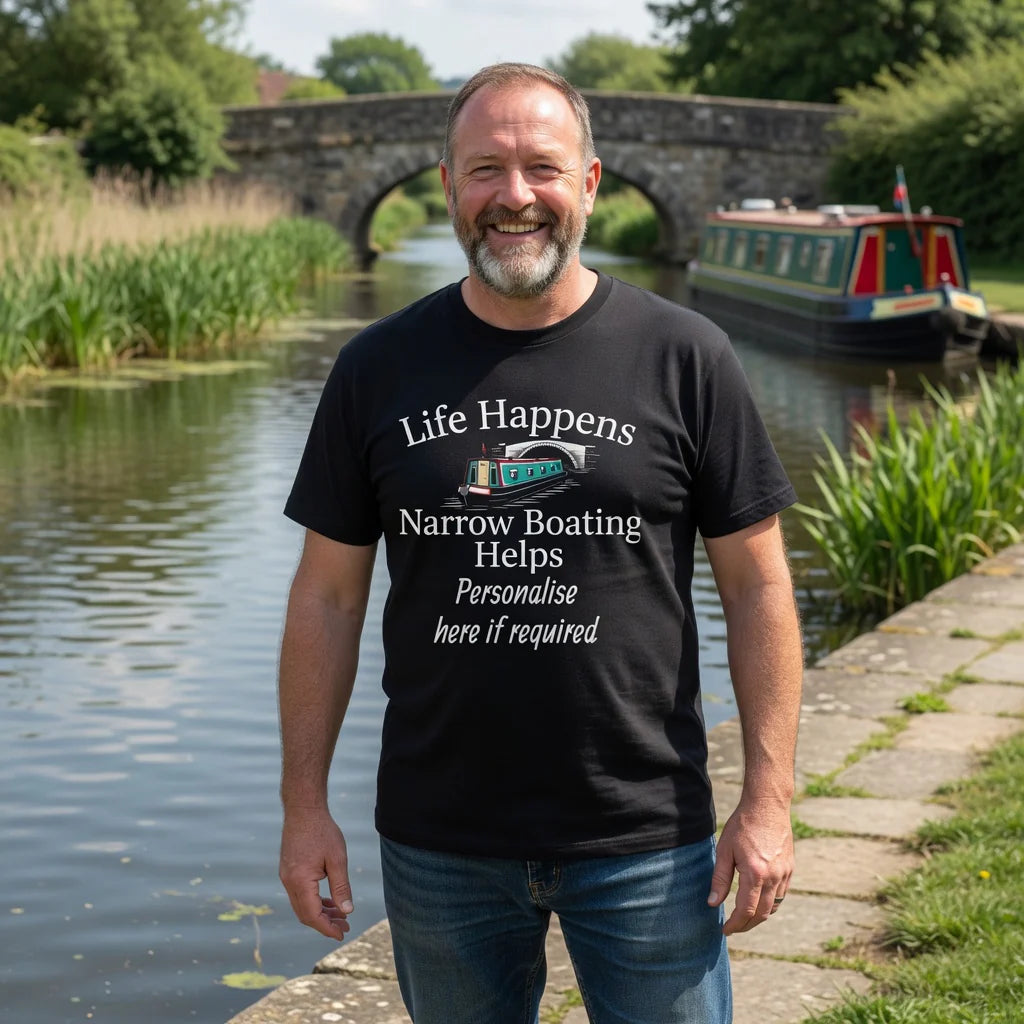 Man wearing a customised black t-shirt with text life happens narrow boating helps standing by a canal with a boat in the background